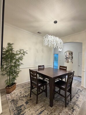 A dining room with a dark wooden table and chairs, a hanging light fixture, a large potted plant, and a rug. - Spacious, bright & modern 3BR+ office in a very safe neighborhood with lakes. (Houston)