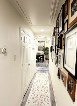 A hallway with a patterned rug, framed pictures on the walls, and a dining area in the background. - Spacious, bright & modern 3BR+ office in a very safe neighborhood with lakes. (Houston)