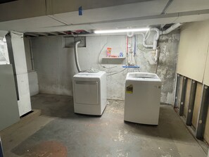 Ein Waschraum mit zwei Waschmaschinen, einem Regal für Reinigungsmittel und freiliegender Sanitärinstallation.