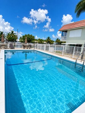 Ein klarer, blauer Pool mit weißem Zaun, Liegestühlen und einem Gebäude mit rotem Dach.
