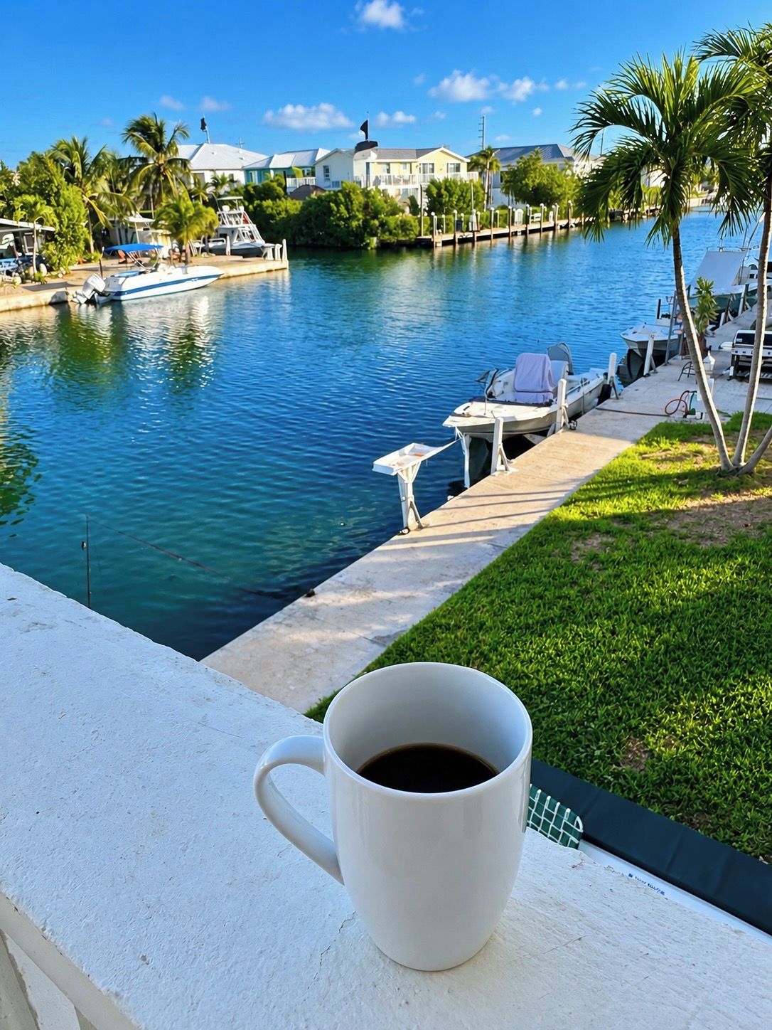 A white mug on a balcony overlooking a marina with boats and a clear blue sky.