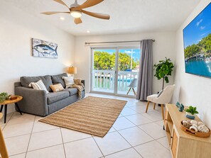 A living room with a sofa, a coffee table, a TV, a ceiling fan, and a view of a pool through the glass door. - Marathon Key Getaway (Marathon)