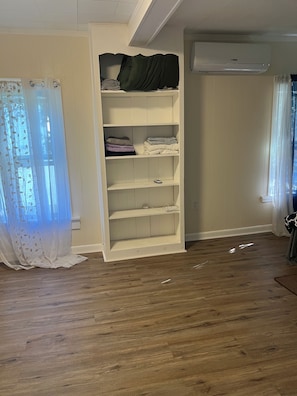 A room with a wooden floor, a white wardrobe with shelves, a curtain, and an air conditioning unit. - Peaceful 2-bedroom house in charming Rutland! Have fun with family & friends (Rutland)