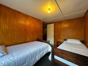 Een kamer met twee houten stapelbedden, een deur en een lamp aan het plafond.