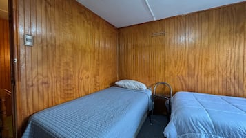 A small, compact room with two single beds, a wooden wall, a small chair, and a wall-mounted light fixture.