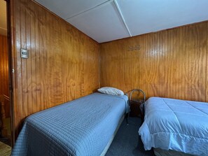 Een kleine, compacte kamer met twee eenpersoonsbedden, een houten wand, een stoeltje en een wandlamp.