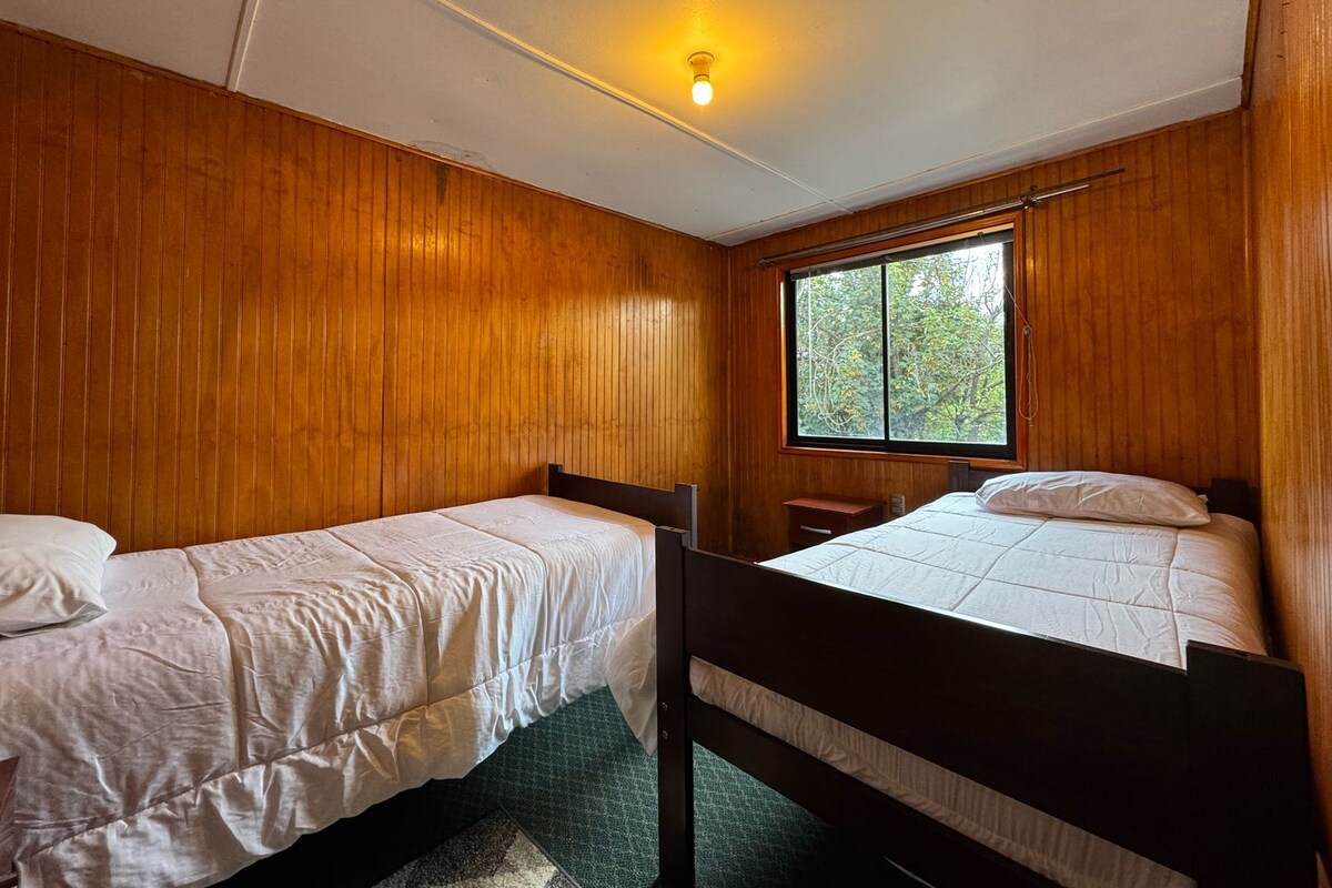 Een kamer met twee eenpersoonsbedden, houten wanden, een raam en een plafondlamp.