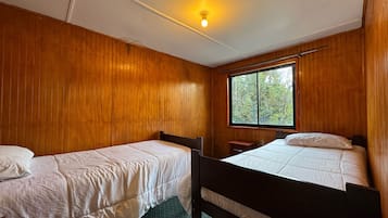 A room with two single beds, wooden walls, a window, and a ceiling light.