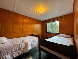 Een kamer met twee eenpersoonsbedden, houten wanden, een raam en een plafondlamp.
