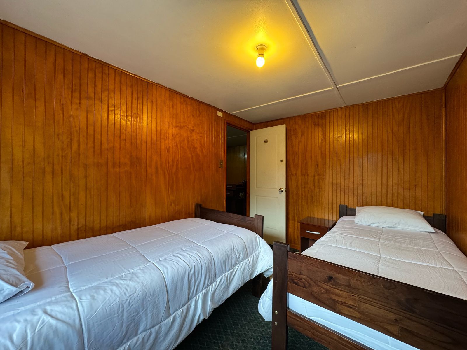 Quarto com duas beliches de madeira, uma porta e um luminário no teto.