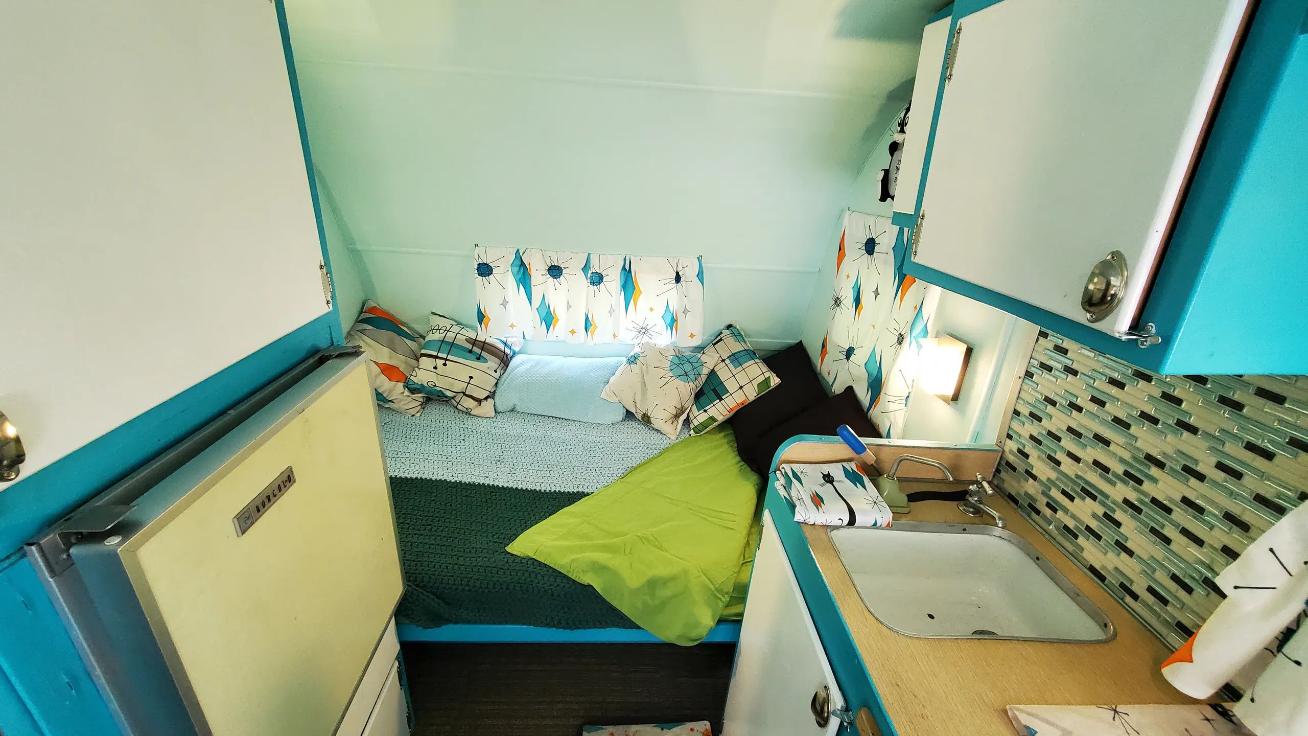 A compact, brightly colored room with a bed, a small sink, and a mirror.