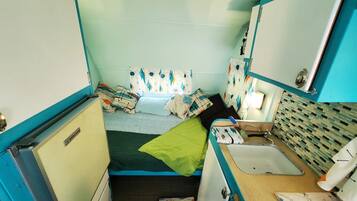 A compact, brightly colored room with a bed, a small sink, and a mirror.