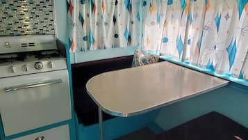 A compact kitchenette with a stove, oven, and a small table with a bench.