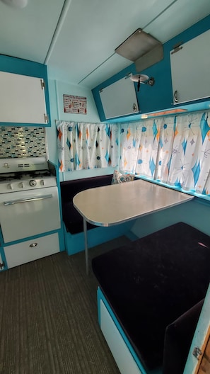 A compact kitchenette with a stove, oven, and a small table with a bench. - The -DaLtOn- (Naches)
