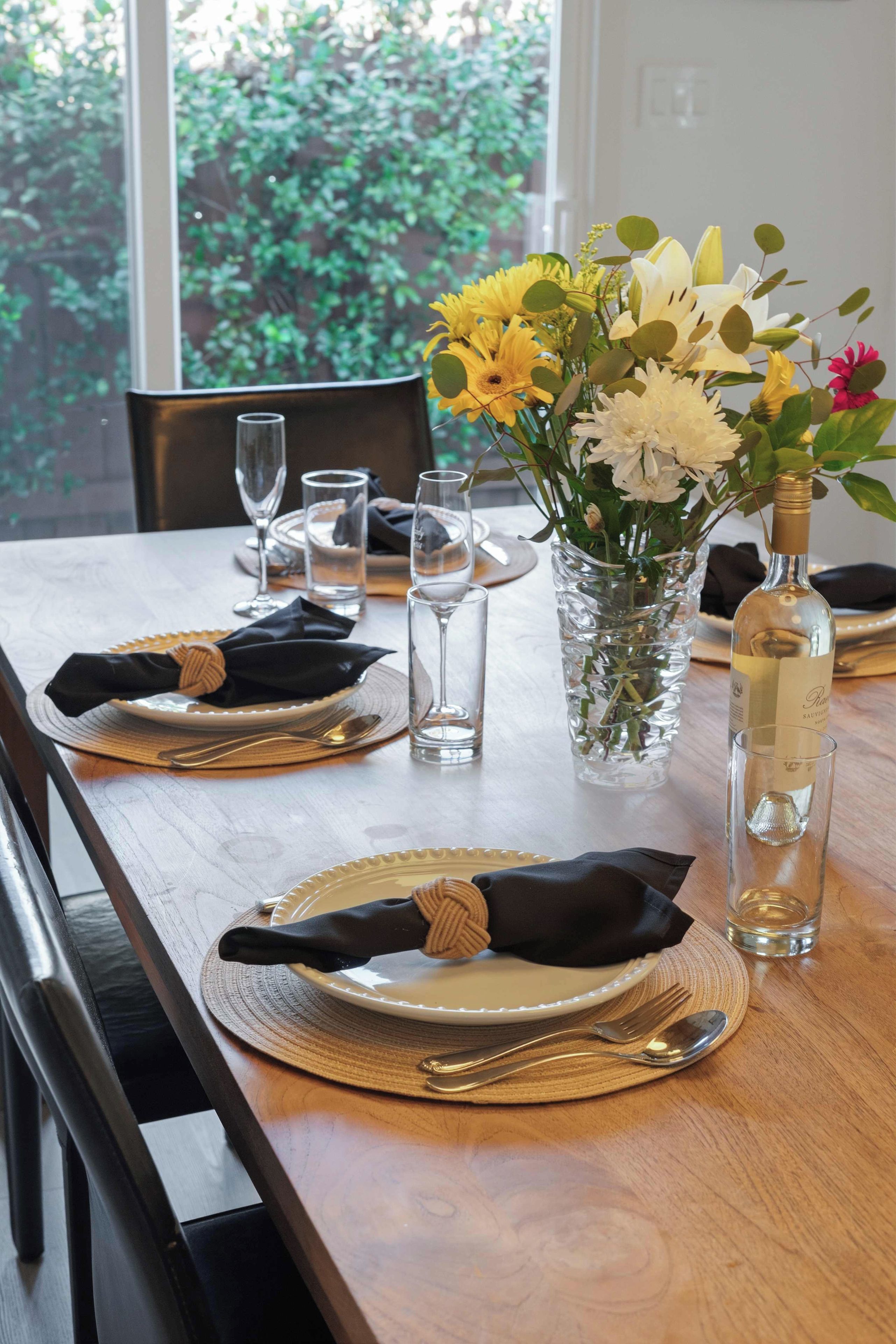 A dining table set with plates, cutlery, glasses, and a vase with flowers.