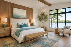 A bedroom with a large bed, two bedside tables, a bench, a chair, a window with a view of trees and water, and a painting on the wall. - Lakefront Paradise 4 king bedrooms, Hot Tub & Private Beach ,fire pit sleeps 12 (Little Elm)