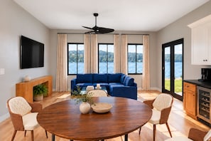 A modern living room with a blue sofa, a wooden dining table, and a view of a lake. - Lakefront Paradise 4 king bedrooms, Hot Tub & Private Beach ,fire pit sleeps 12 (Little Elm)