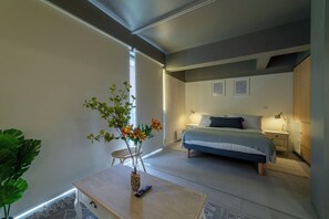 Un dormitorio con cama, mesitas de noche y una pequeña mesa con un florero y control remoto.