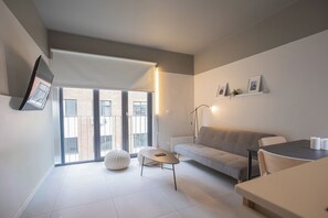 A modern living room with a sofa, a round ottoman, a small table, and a dining area with a table and chairs. - Bright 1-room apartment + large window · Featured (H16)   (Providencia)