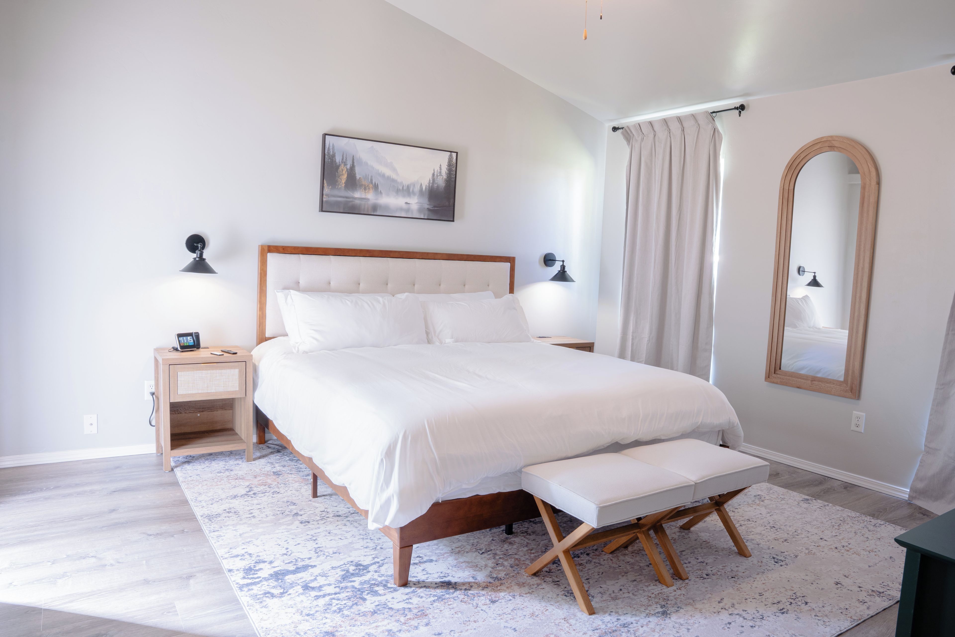 Une chambre à coucher comprenant un lit, des tables de chevet, une commode, un banc, un miroir et un tableau accroché au mur.