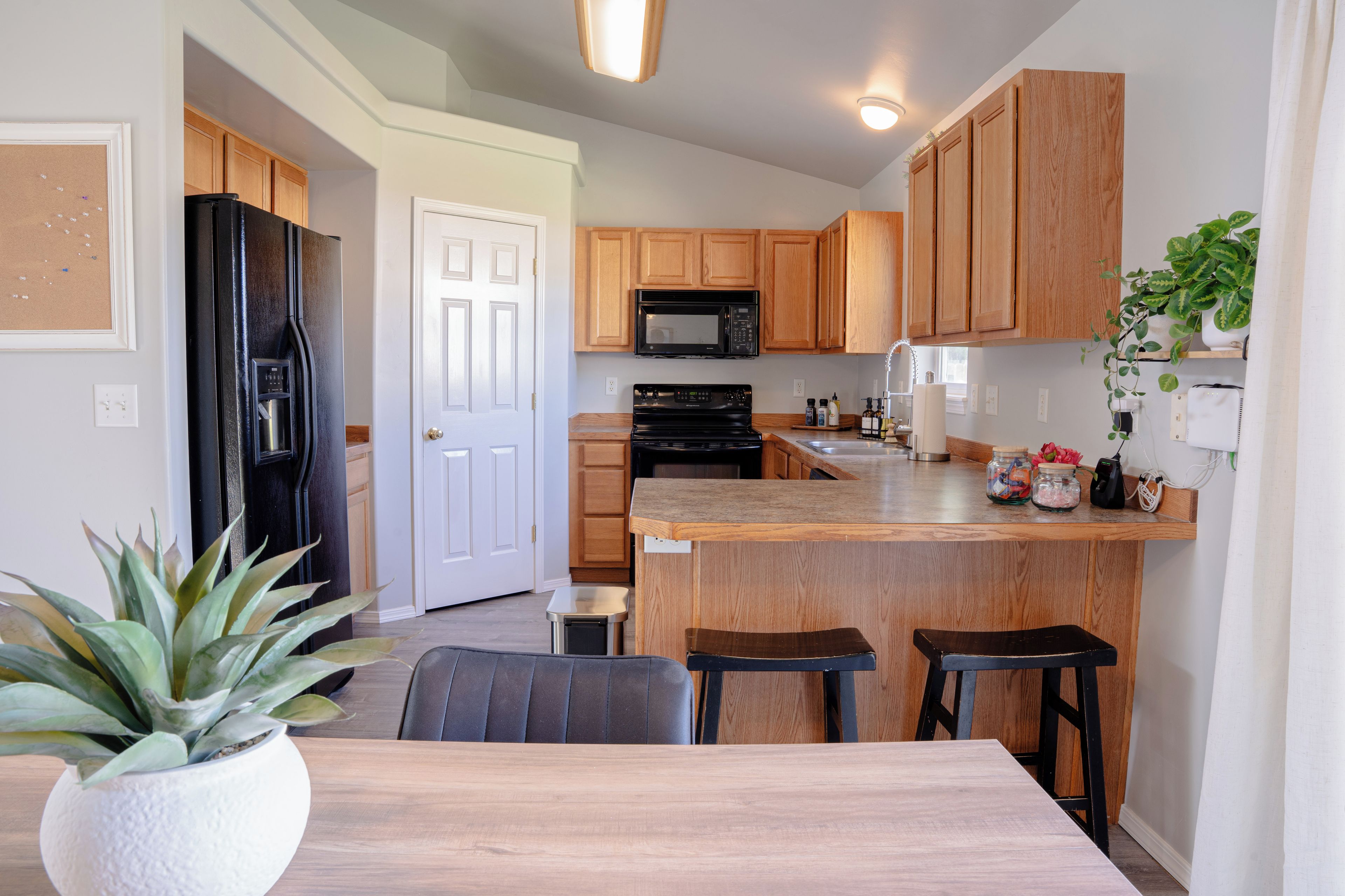 Una cocina moderna con armarios de madera, un refrigerador negro, un microondas y un lavamanos de acero inoxidable.