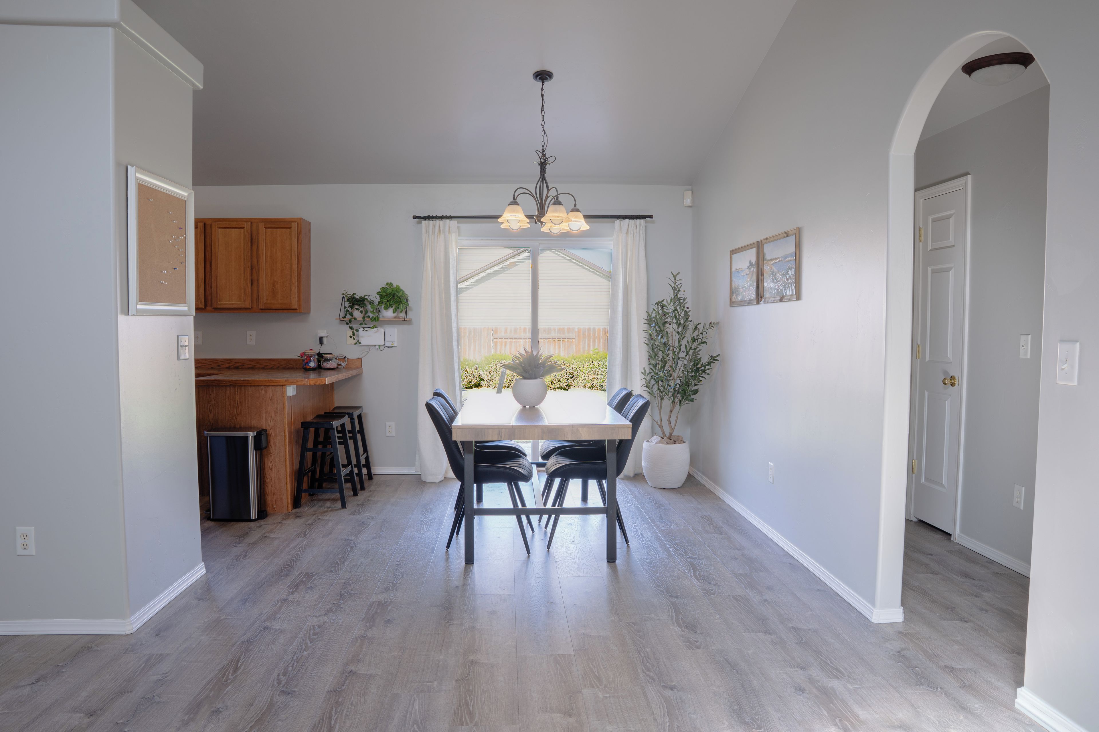 Une cuisine moderne avec des meubles en bois, une table à manger avec des chaises, un luminaire suspendu et une vue par la fenêtre.