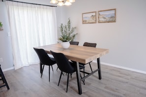 Un comedor con una mesa de madera, sillas negras, un florero blanco con una planta y dos cuadros en la pared.