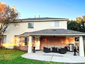 Una casa con porche cubierto, mobiliario exterior y una parrilla.