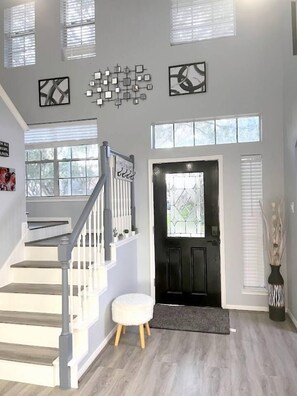 A staircase leading to a landing with a black door, a white bench, and a wall-mounted light fixture. - Modern 4BR Retreat Extended Stay Ideal. SW Houston (Sugar Land)