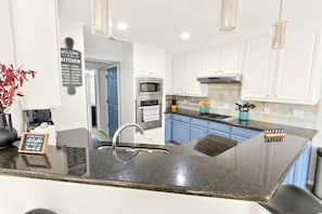 Una cocina moderna con armarios blancos, encimera de granito y electrodomésticos de acero inoxidable.