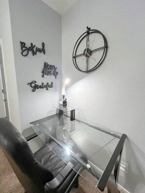 Ein Zimmer mit einem Glastisch, einem schwarzen Ledersessel und einer Wanduhr.