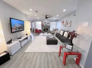 A modern living room with a flat-screen TV, a sofa, a glass coffee table, and a fireplace. - Modern 4BR Retreat Extended Stay Ideal. SW Houston (Sugar Land)