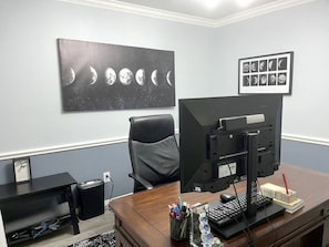 Una oficina en casa con un escritorio, computadora y un cuadro colgando en la pared con las fases de la luna.