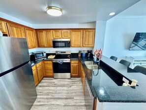 A modern kitchen with wooden cabinets, stainless steel appliances, and a black granite countertop. - Balcony Lake Views | Pool, Gym, WiFi & Parking (Orlando)