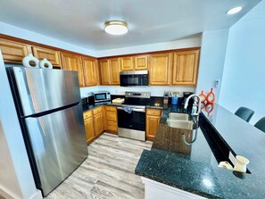 A modern kitchen with wooden cabinets, stainless steel appliances, and a granite countertop. - Balcony Lake Views | Pool, Gym, WiFi & Parking (Orlando)