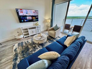 A modern living room with a blue sofa, a round coffee table, and a flat-screen TV mounted on the wall. - Balcony Lake Views | Pool, Gym, WiFi & Parking (Orlando)