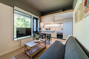 A compact living space with a sofa, a dining area, a kitchen, and a window with a view of greenery. - Bright Studio · Selected Design (H17) (Providencia)