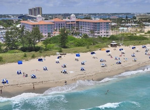 A beach with multiple umbrellas and sun loungers, a building with a red roof, and a view of the ocean. - Oceanfront 2 Bedroom Unit for 6 people at Palm Beach Shores Resort Singer Island (Palm Beach Shores)