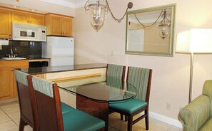 A kitchen with wooden cabinets, a refrigerator, a microwave, and a dining area with a glass table and wooden chairs. - Oceanfront 2 Bedroom Unit for 6 people at Palm Beach Shores Resort Singer Island (Palm Beach Shores)