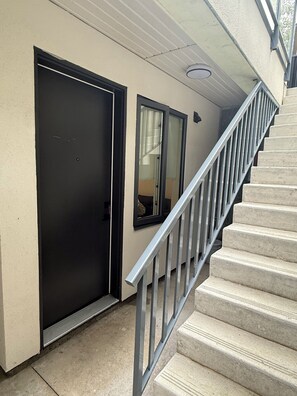 Una escala amb barana de metall que condueix a un pis superior, una porta negra i una finestra amb vista a l'interior.