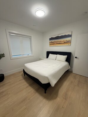 A bedroom with a bed, a window, a painting, and a door. - Spacious 2BR Suite| Walk to White Rock Beach (White Rock)