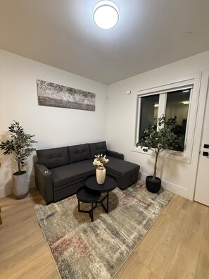A modern living room with a sectional sofa, a round coffee table, and two potted plants. - Spacious 2BR Suite| Walk to White Rock Beach (White Rock)