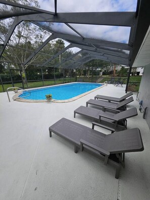 A covered outdoor area with a swimming pool, lounge chairs, and a pergola structure. - Beautiful Historical 6 Bdrm Lakefront Pool Home (Auburndale)