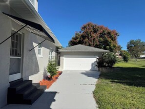 A residential house with a garage, a front yard with a small tree, and a clear blue sky. - Beautiful Historical 6 Bdrm Lakefront Pool Home (Auburndale)