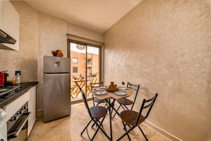 A compact kitchen with a refrigerator, stove, and dining area with chairs and a table. - Moroccan Style Apartment in Gueliz – Near Carré Eden Mall (Marrakesh)