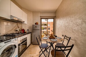 A compact kitchen with a gas stove, oven, washing machine, and a refrigerator. There is a dining area with a table and chairs. - Moroccan Style Apartment in Gueliz – Near Carré Eden Mall (Marrakesh)