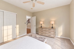 A bedroom with a bed, a dresser, two lamps, a ceiling fan, and a door leading to a staircase. - The Westfield Retreat | 7 Bedrooms • 30+ Day Stays (Westfield)