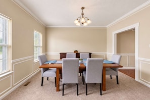A dining room with a wooden table, six grey chairs, a chandelier, and beige walls. - The Westfield Retreat | 7 Bedrooms • 30+ Day Stays (Westfield)