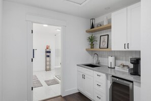 A modern kitchen with white cabinetry, a built-in dishwasher, a coffee maker, and a plant on a shelf. - Booje Bay : Luxury, Lakefront, Hot Tub! (Sunrise Beach)