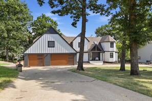 A residential property with a garage, a covered porch, and a driveway leading to the entrance. - Booje Bay : Luxury, Lakefront, Hot Tub! (Sunrise Beach)